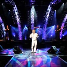 A man in white stands on stage with lights.