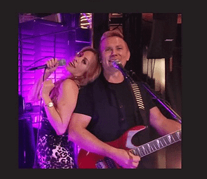 A man and woman are playing guitar in front of a microphone.