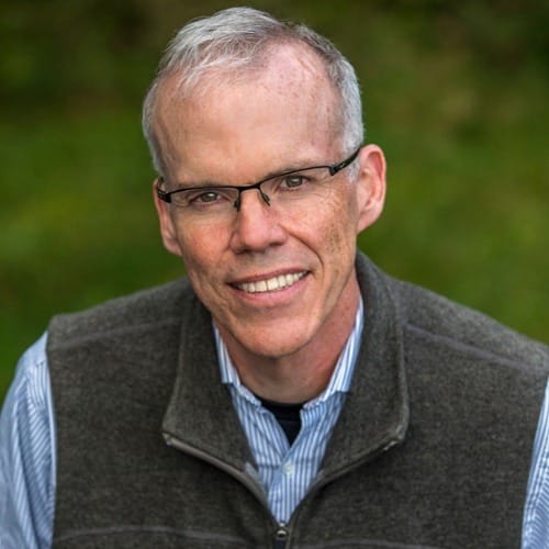 A man with glasses and a vest smiling for the camera.